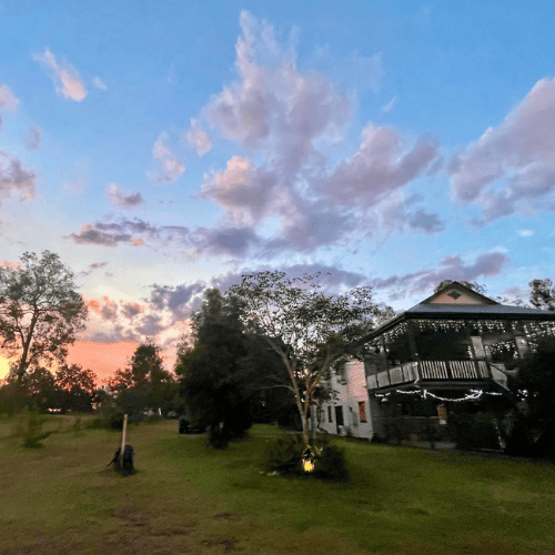 bnb in lockyer valley with sun setting to the left of the house making the clouds orange in that section of sky. fairy lights decorate the bnb