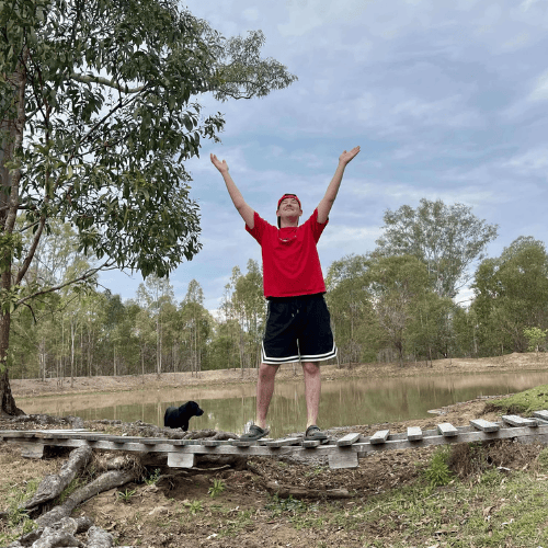 Teen with red shirt standing on bridge over dam with dog in background at content creator venue in lockyer valley